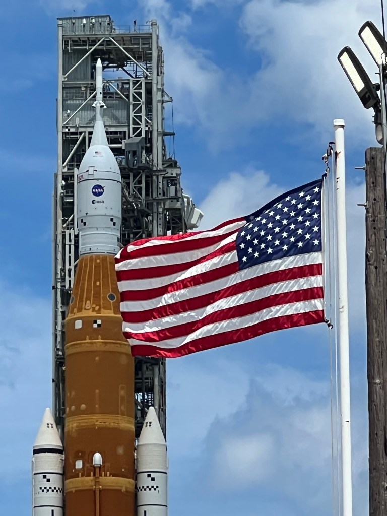 Close-up of NASA's SLS Rocket, an American flag billows in the foreground.