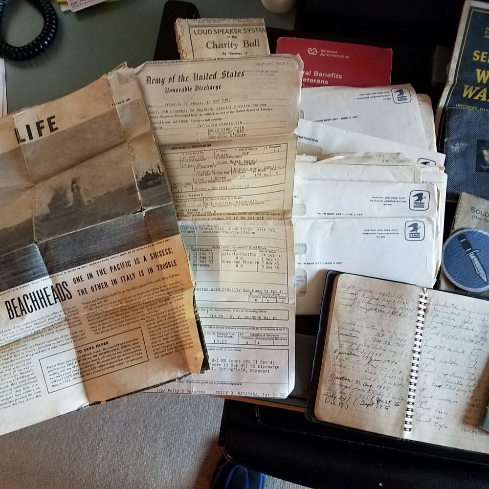 A pile of envelopes, ads, letters, magazines, an honorable discharge notice, and an open journal illustrates Thorness's research.