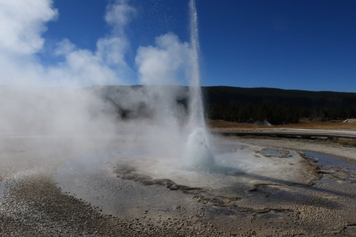 Water and spray shoot up into a dark blue sky with white steam floating off to the left.