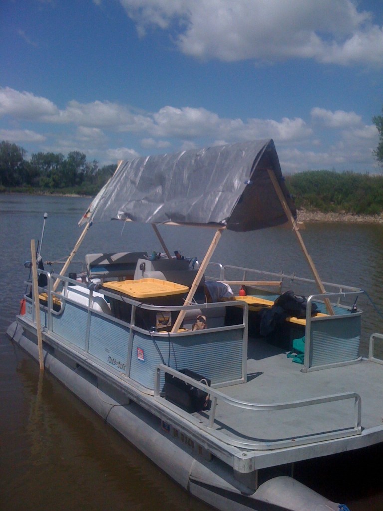 Author’s aged pontoon boat, which has a cheaply constructed A-frame tarp shading the deck, that she and her companions used to float the river.