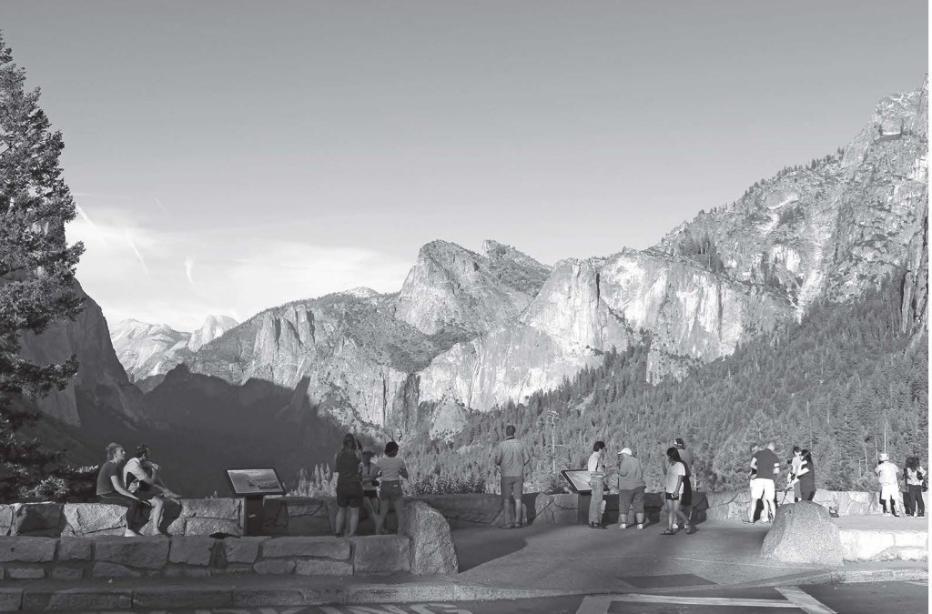 A group of people stand in front of interpretive signs, with a large valley in front of them, and rock formations on each side.